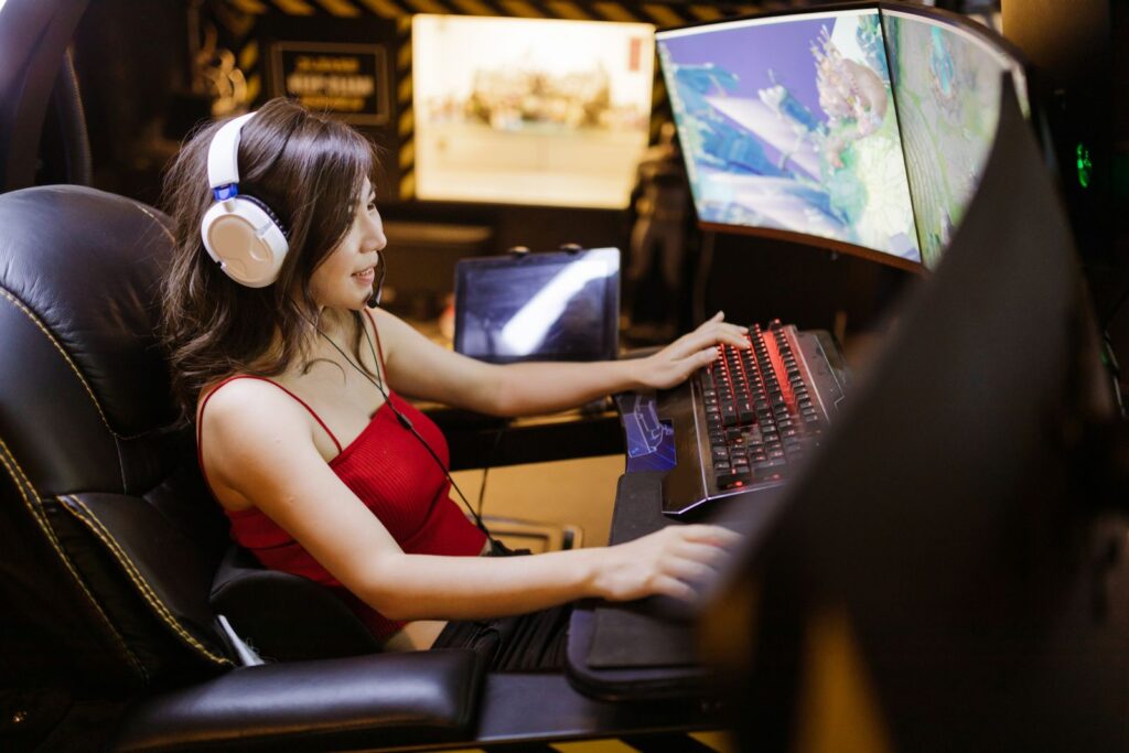 A woman engaged in video gaming on a high-tech computer setup with multiple monitors and headphones.