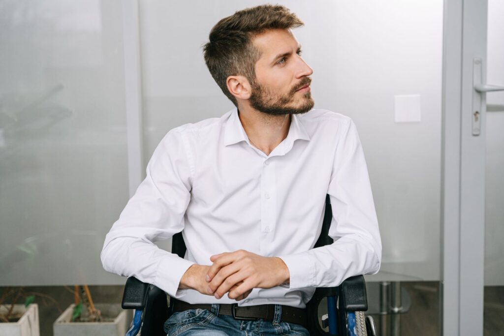 Stylish young man with a beard sitting in a wheelchair. Modern office setting, thoughtful expression.