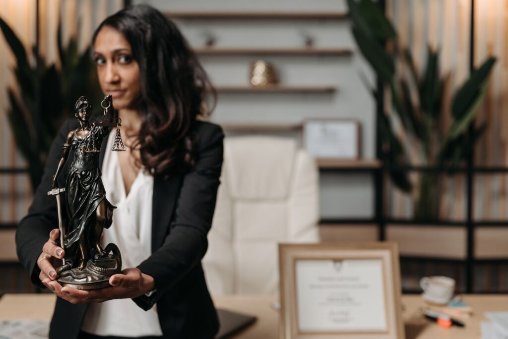 A female lawyer presenting a Lady Justice statue in a modern office setting.