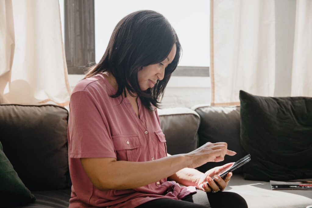 Woman in pink shirt using a smartphone while sitting on a couch, side view.