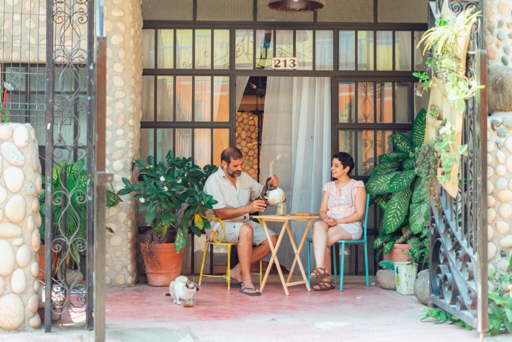 Couple enjoying tea on a charming patio surrounded by lush plants and warm atmosphere.