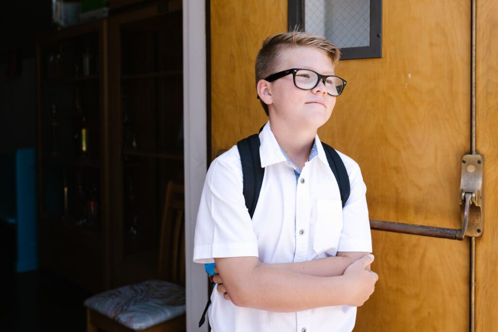 Confident student standing with arms crossed at school entrance, ready for a new day.