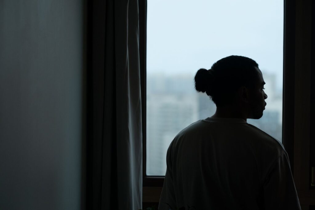 Silhouette of a man with ponytail gazing through a window with a blurred cityscape view.