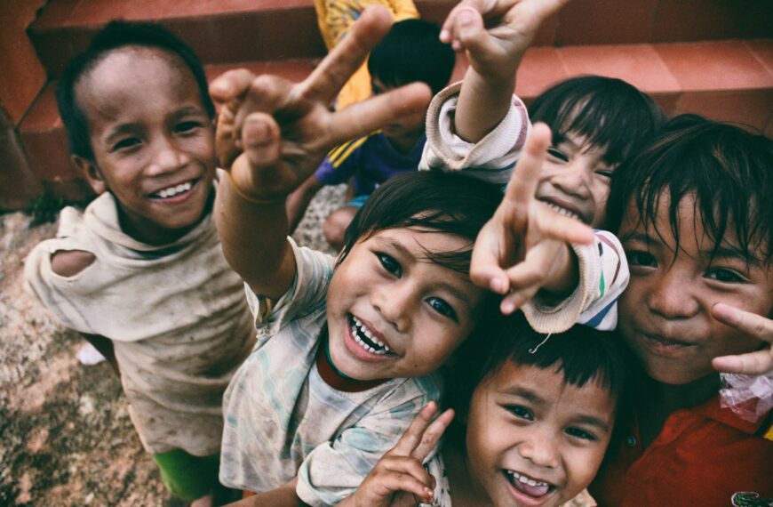 five children smiling while doing peace hand sign