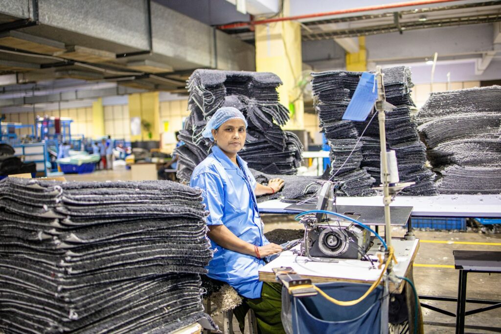 A factory worker sits surrounded by stacks of materials.