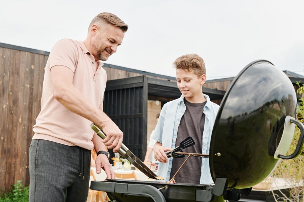 A father and son grilling together outdoors on a sunny day in the backyard
