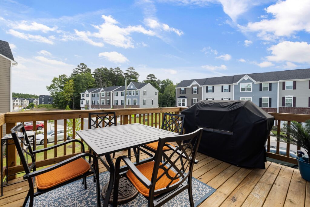 Wooden backyard deck with table, chairs, and grill overlooking a suburban neighborhood