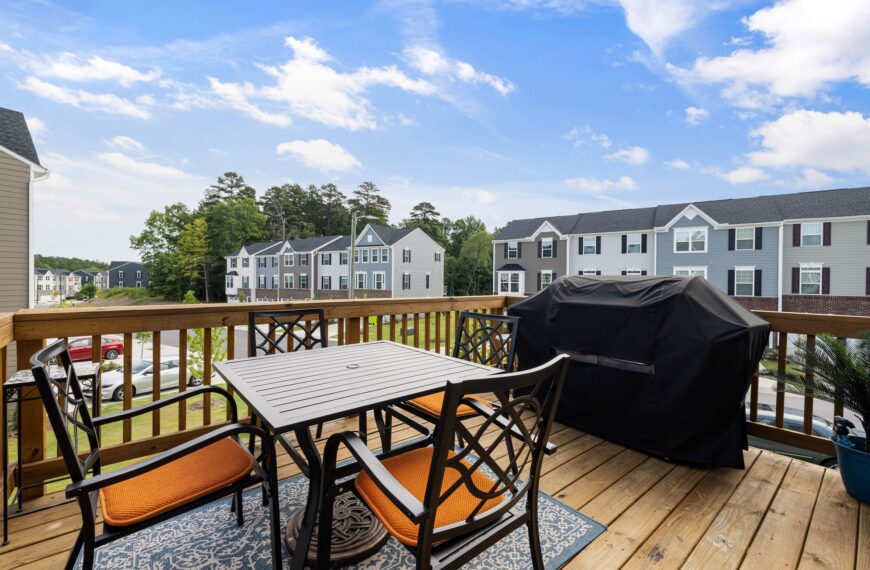 Wooden backyard deck with table, chairs, and grill overlooking a suburban neighborhood
