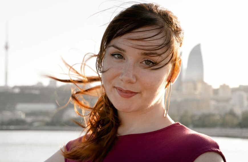 Young woman with windblown hair smiles against a city skyline.