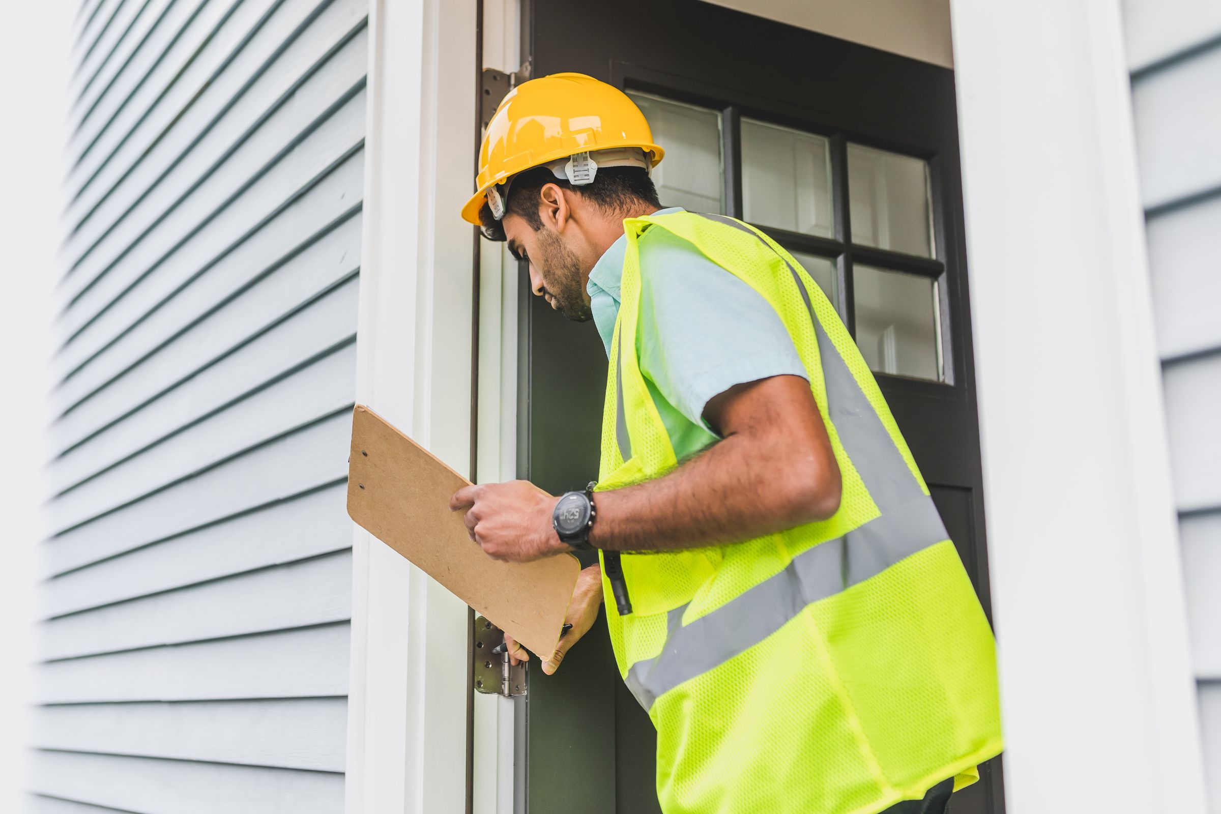 Contractor in a hard hat and safety vest holding a clipboard during a residential home inspection