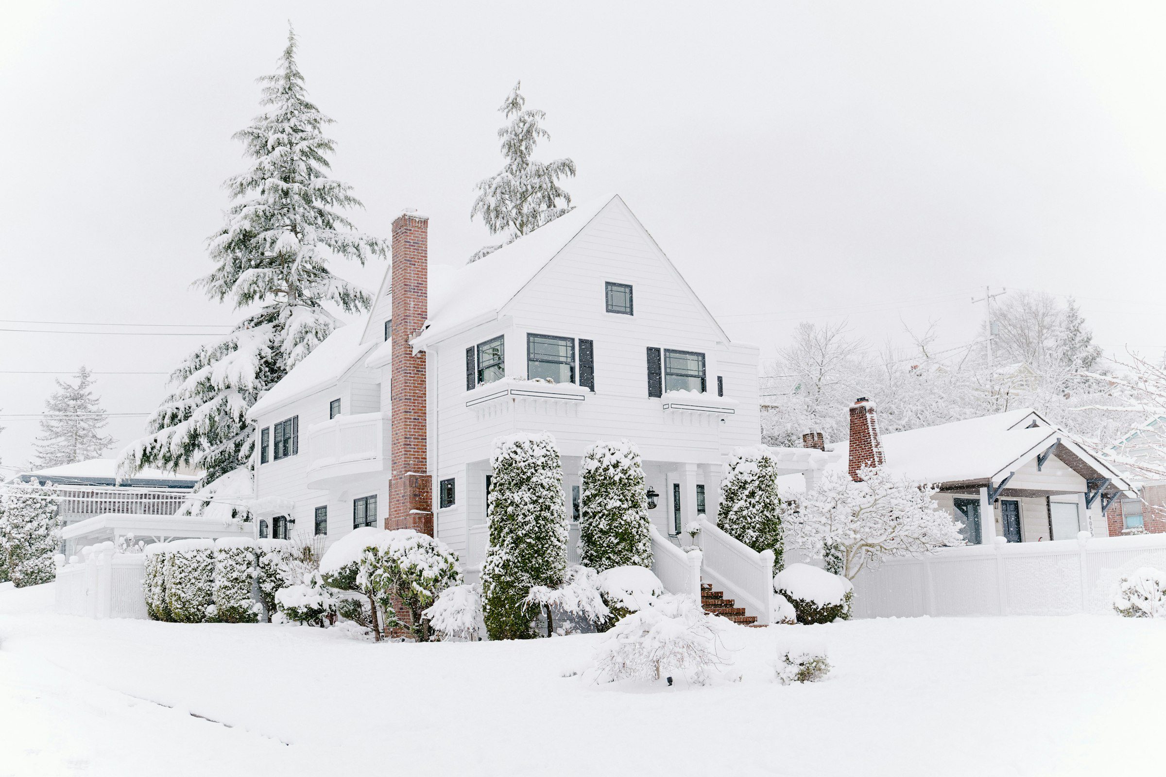 A brick home with a chimney and snow-dusted evergreens, illustrating a house ready for winter weather