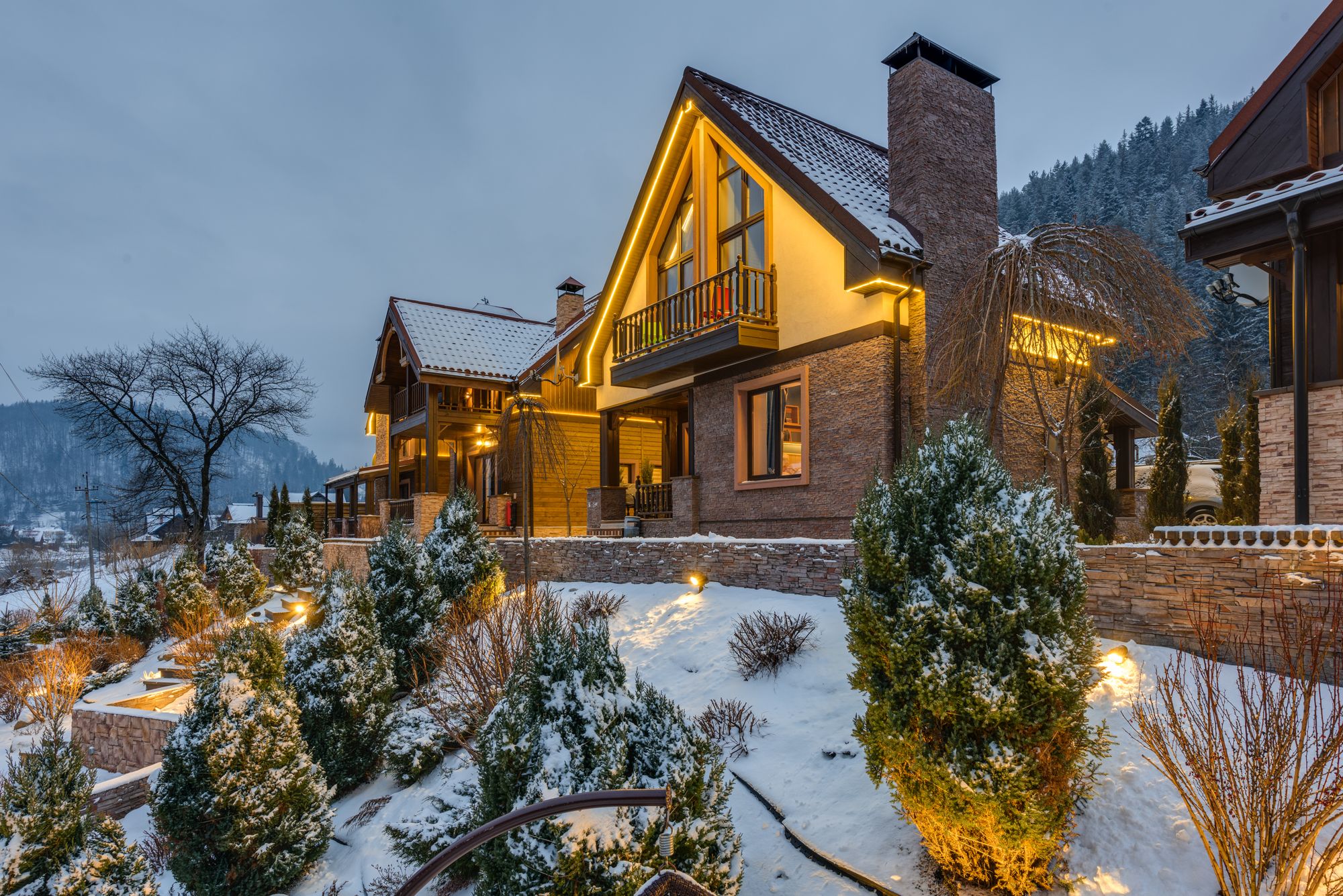 A cozy, warmly lit home exterior surrounded by snow-covered trees in winter, representing a well-prepared, winterized house