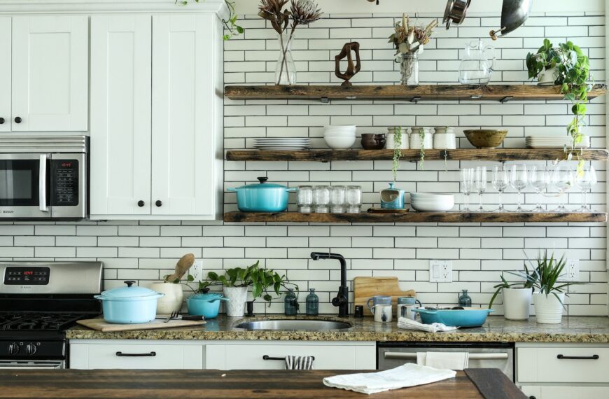A kitchen with white cabinets, subway tile, and open wooden shelves holding cookware