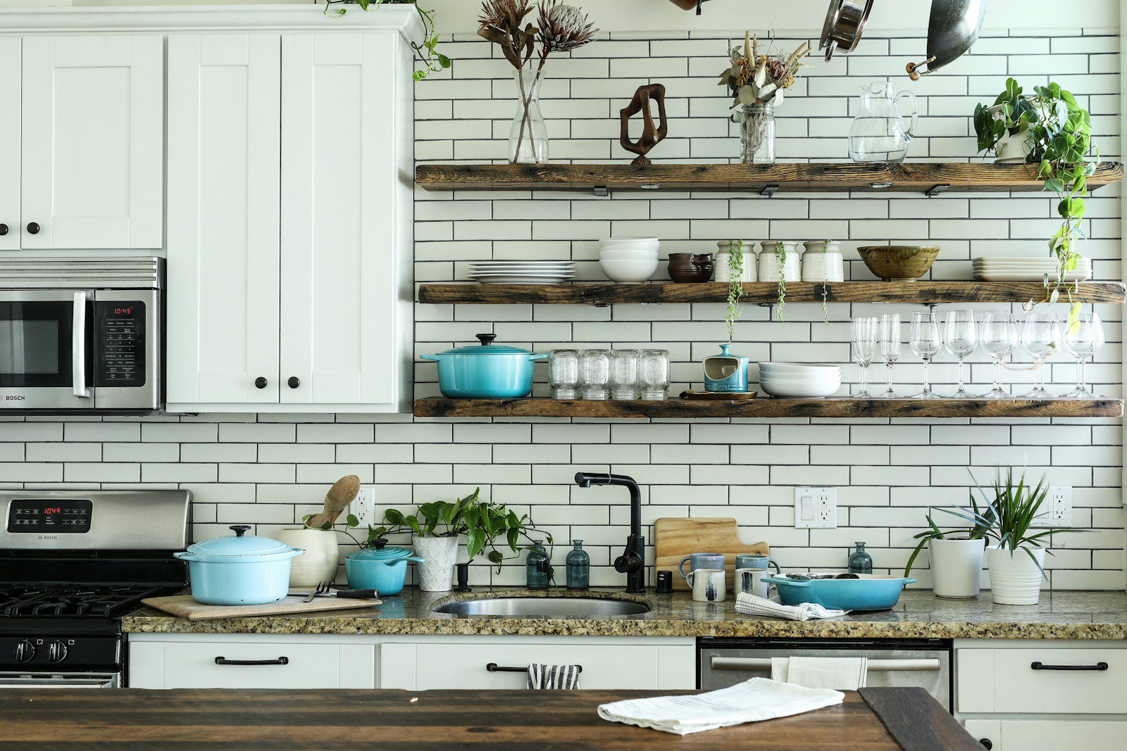 A kitchen with white cabinets, subway tile, and open wooden shelves holding cookware