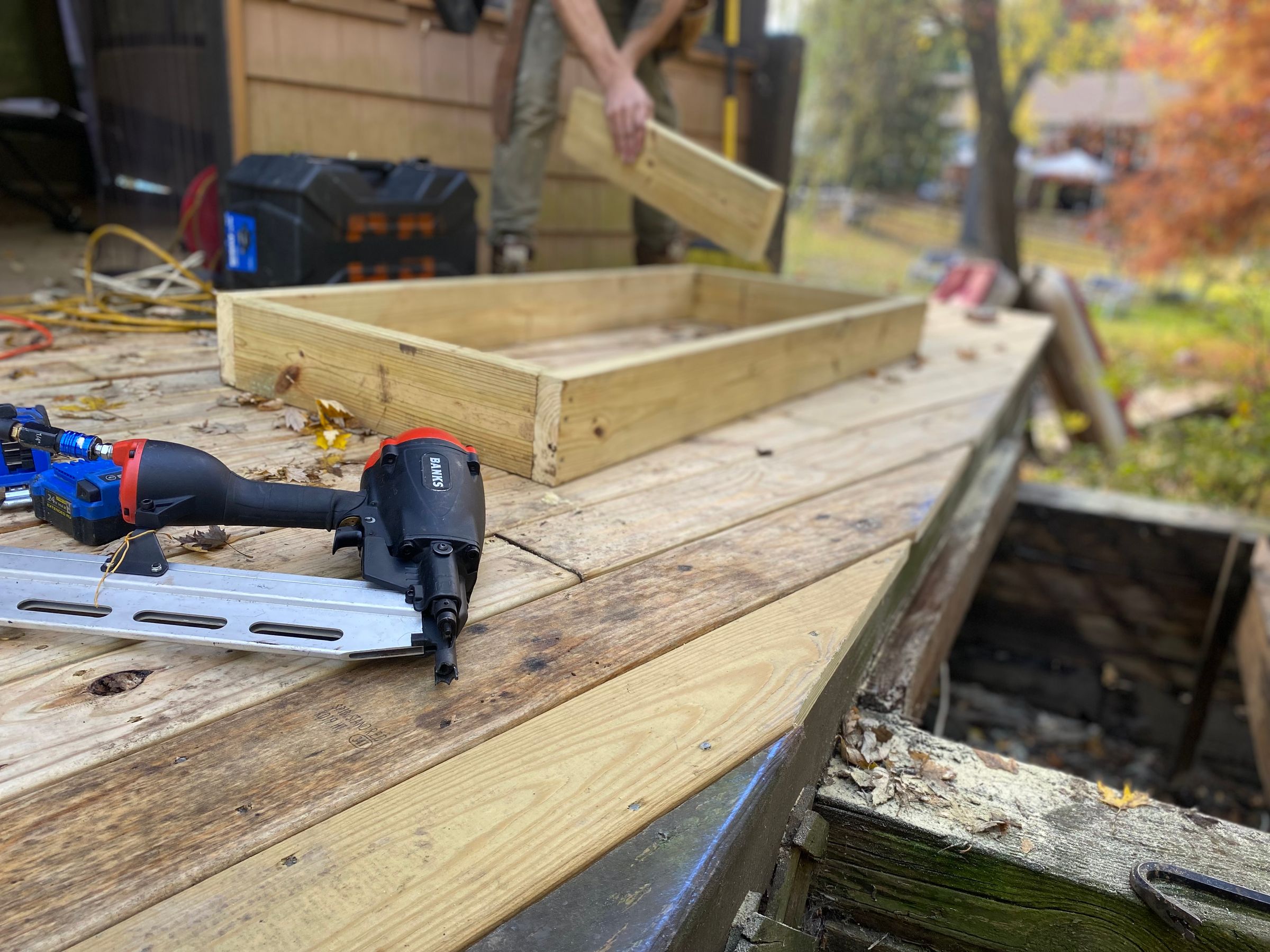 Close-up of a pneumatic nail gun securing wooden deck boards during construction