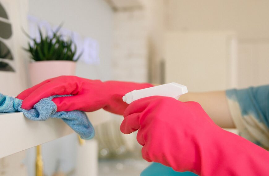 Person spraying a natural cleaning solution on a bright kitchen shelf while wiping with a cloth