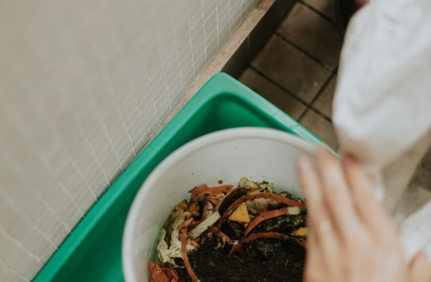 Hands adding fresh food scraps into a compost bin filled with dark, rich soil