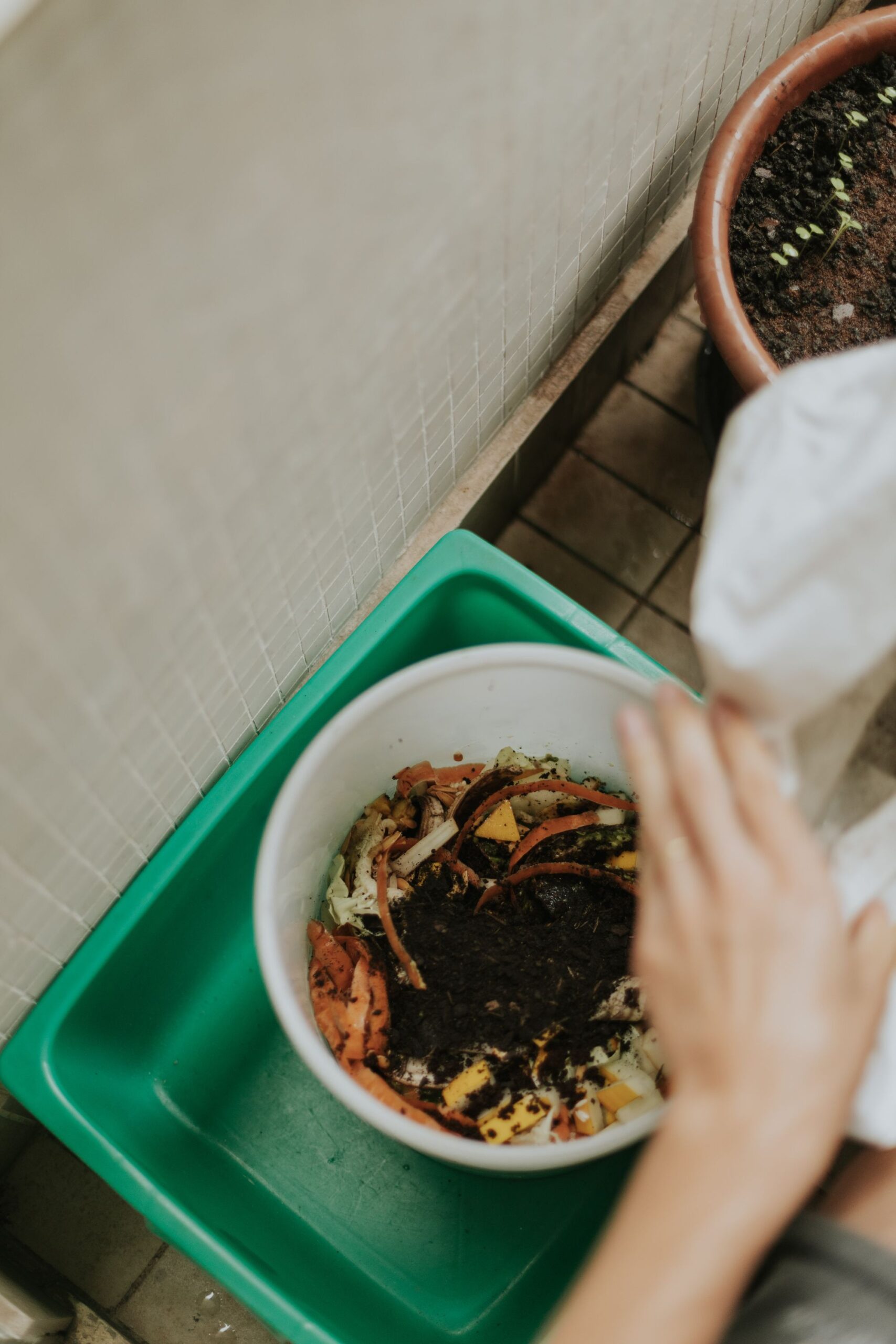 Hands adding fresh food scraps into a compost bin filled with dark, rich soil