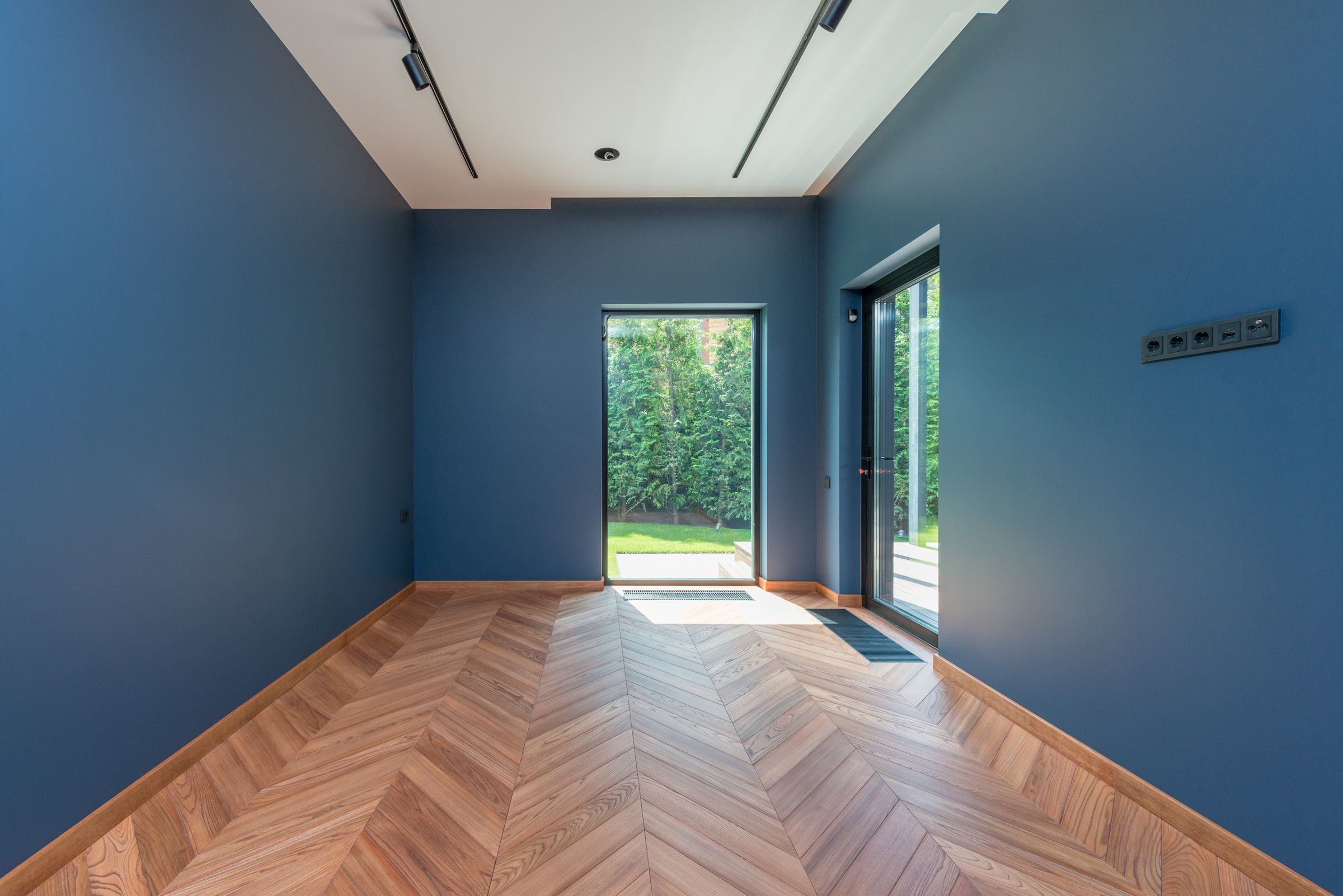 Bright living room with blue walls and a warm-toned herringbone hardwood floor leading to glass garden doors