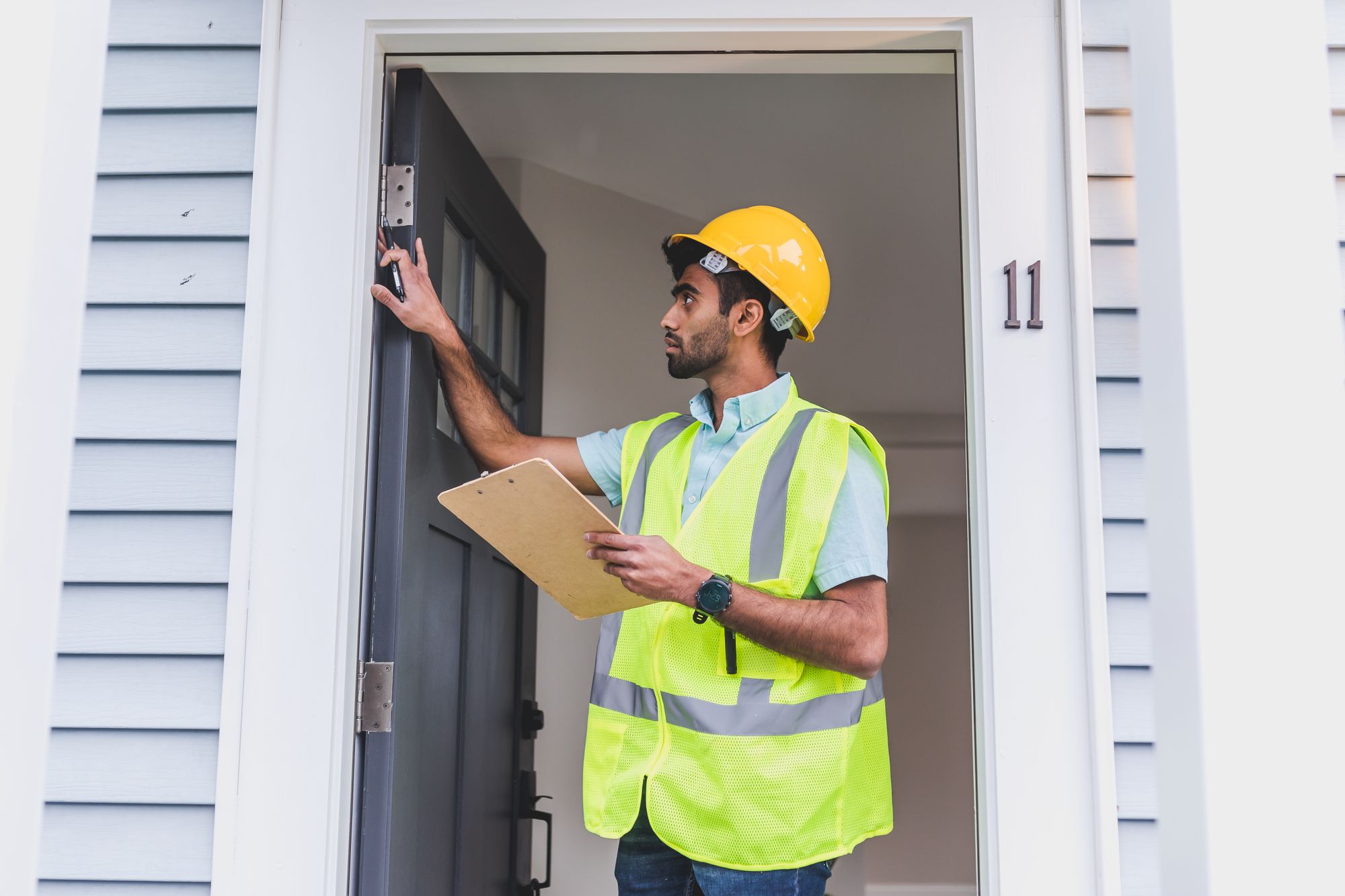 Inspector in a safety vest and hard hat checking a home's front entrance and foundation for damage