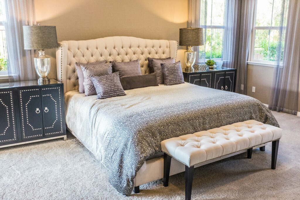 A tufted headboard bed with grey patterned bedding and a cream bench in a bedroom