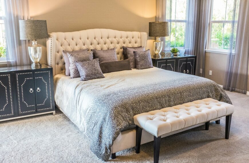 A tufted headboard bed with grey patterned bedding and a cream bench in a bedroom