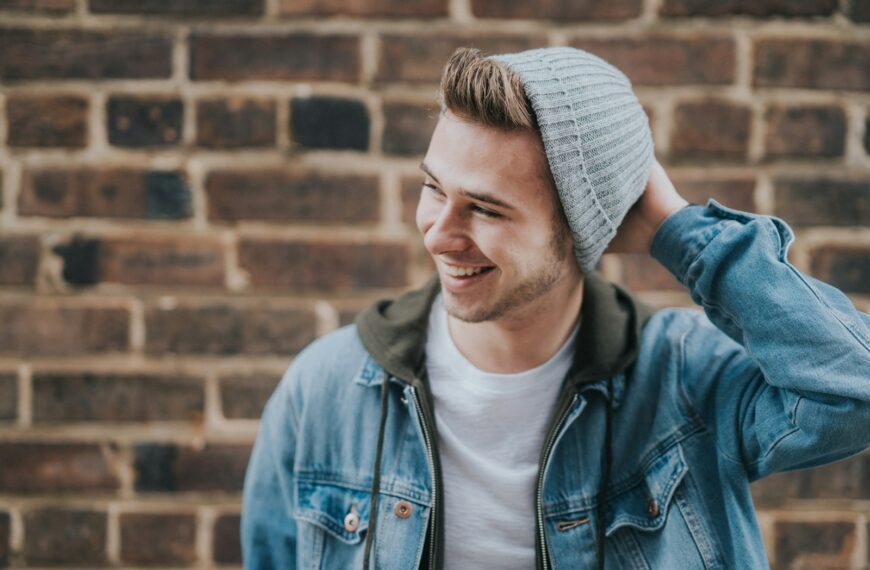 man holding the back of his head while smiling near brick wall