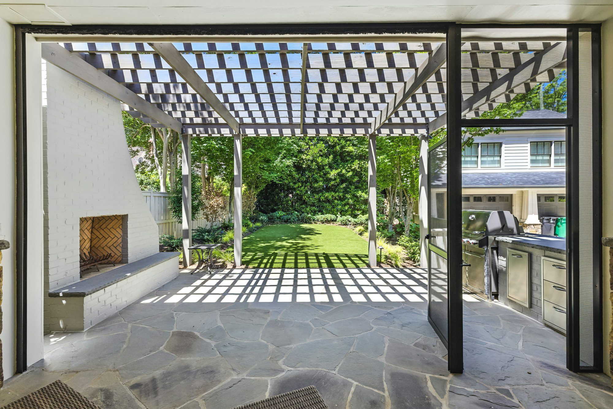 Modern backyard outdoor living space with a pergola, fireplace, and outdoor kitchen zone