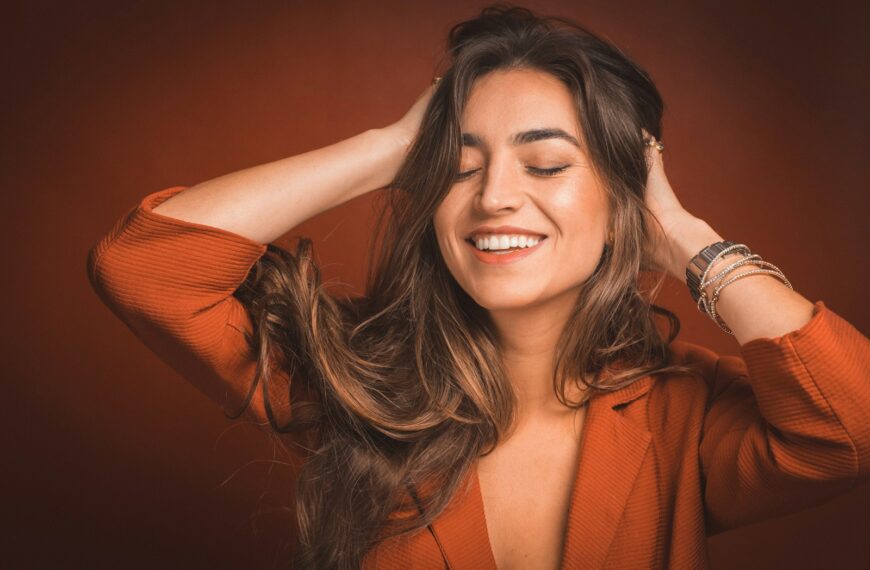 smiling woman in brown top holding hairs