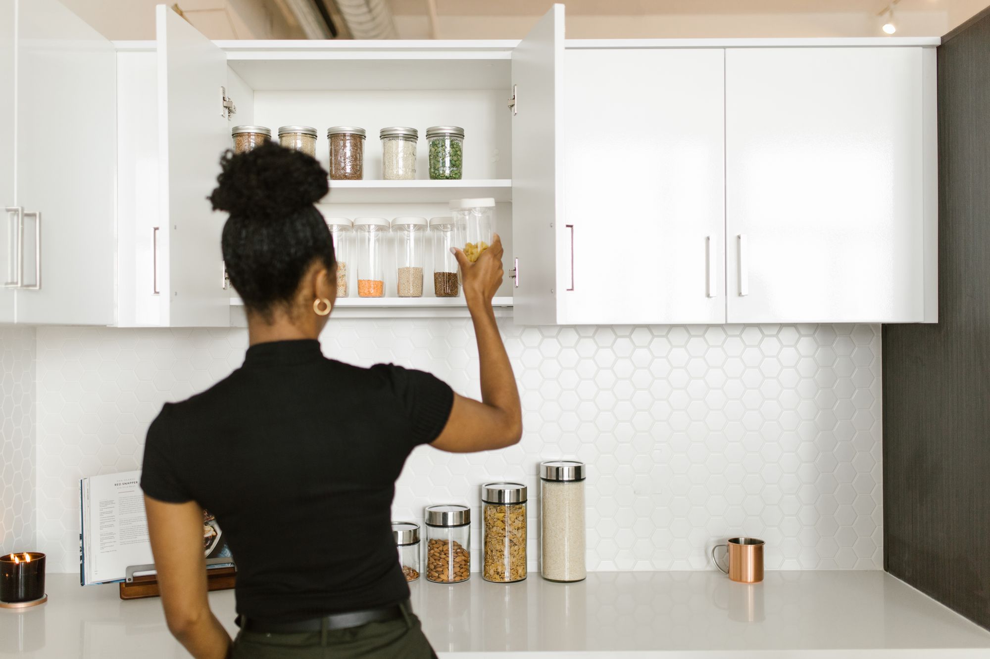 Woman organizing a pantry shelf lined with labeled glass jars, reflecting the booming professional organizing industry