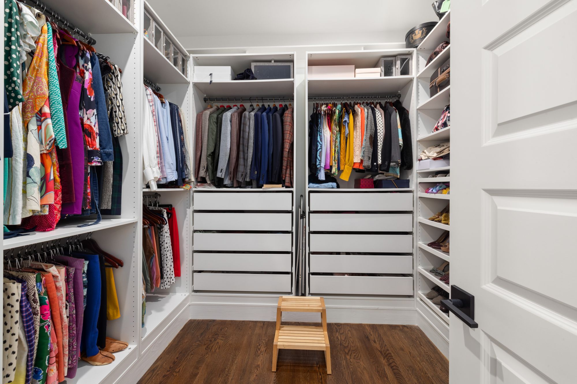 A neatly organized walk-in closet with colorful clothes, shoes, and accessories arranged on racks and shelves