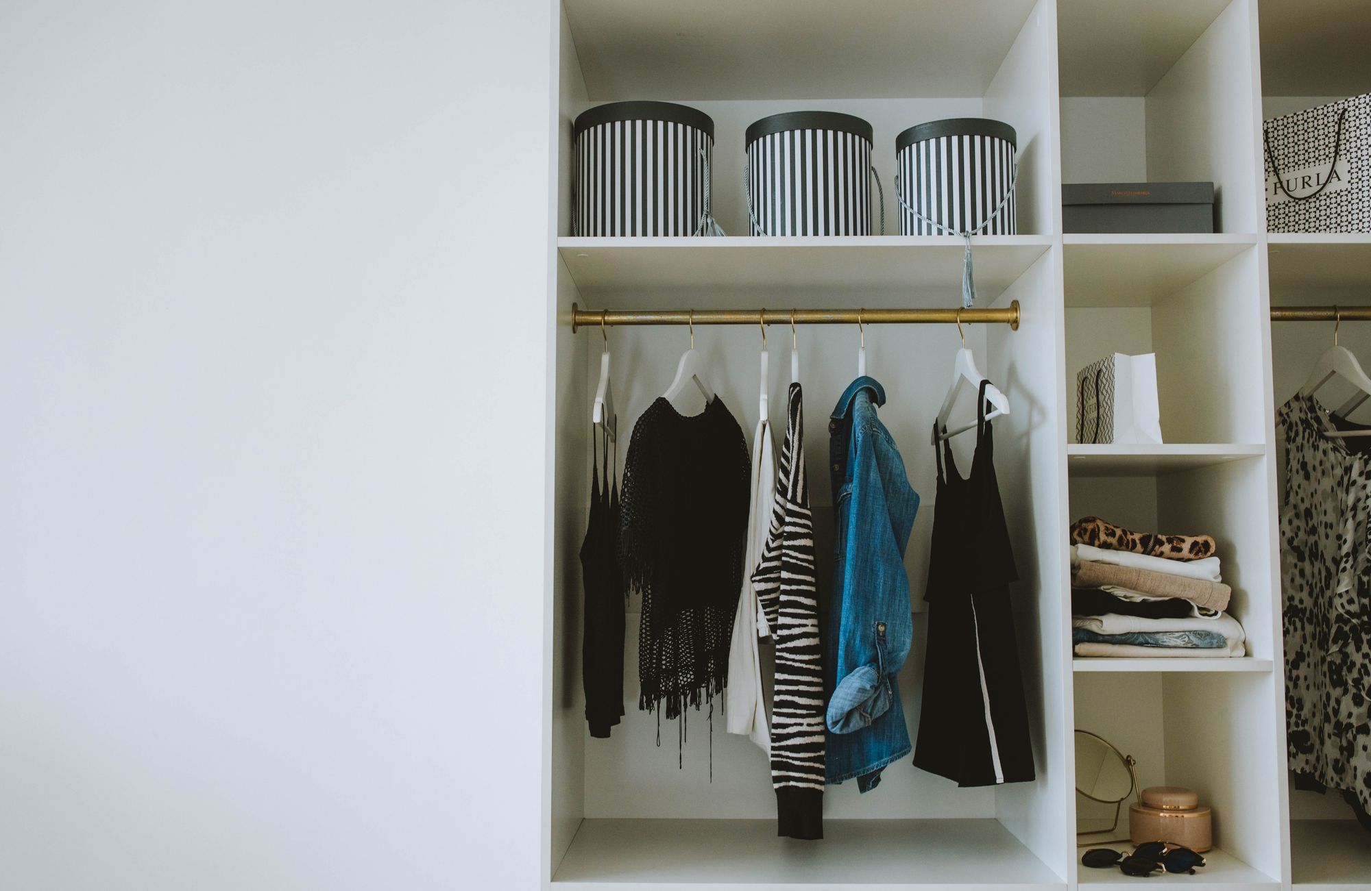 A neatly organized wardrobe with clothes on hangers and striped storage boxes on a shelf