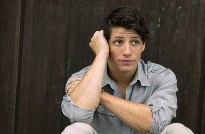 man wearing gray dress shirt leaning on brown wall