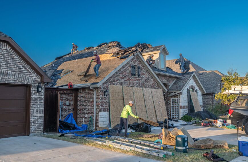 Construction workers replacing shingles on a residential roof in daylight