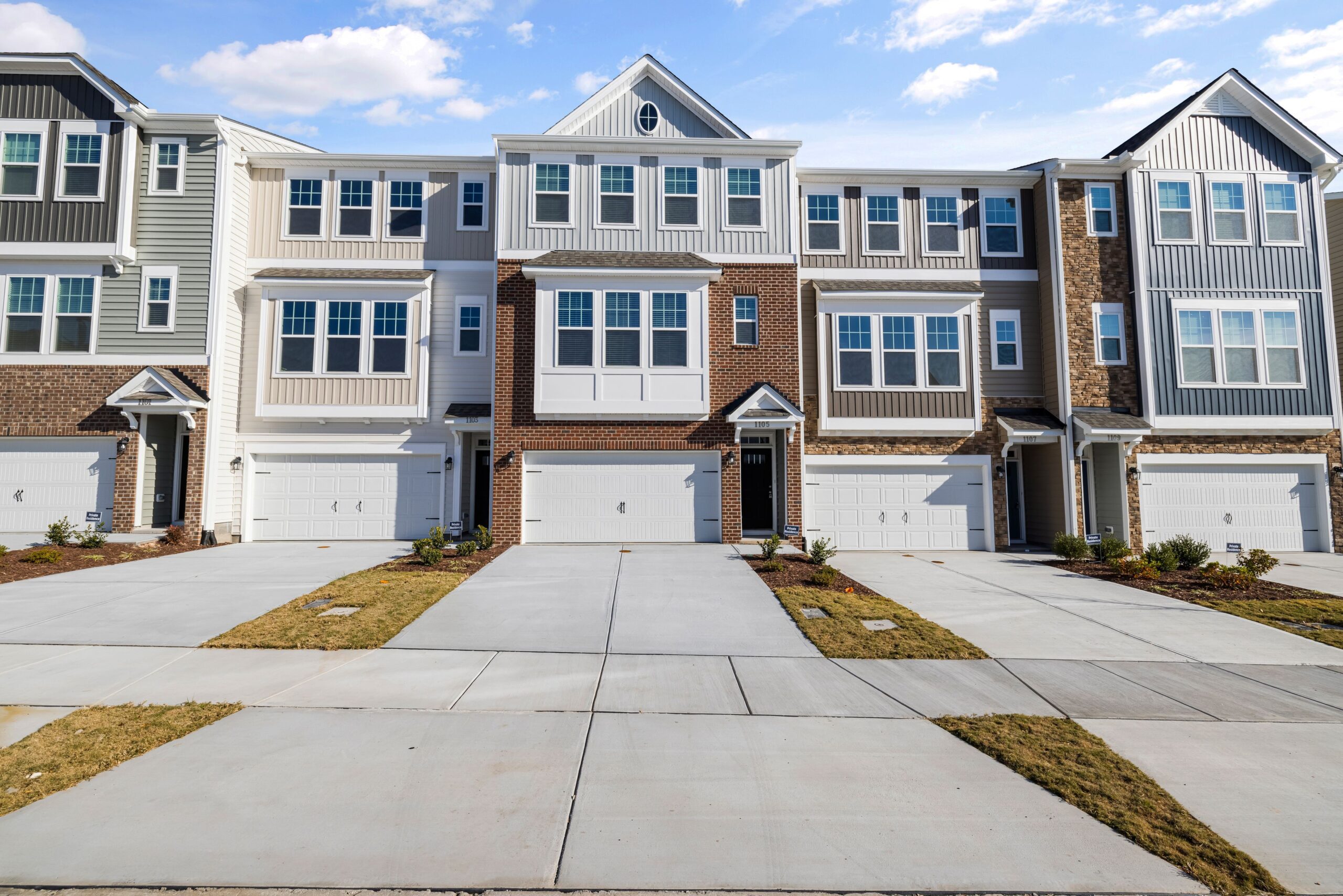 Row of modern townhouses with spacious driveways and garage fronts under a blue sky, representing an HOA-governed community