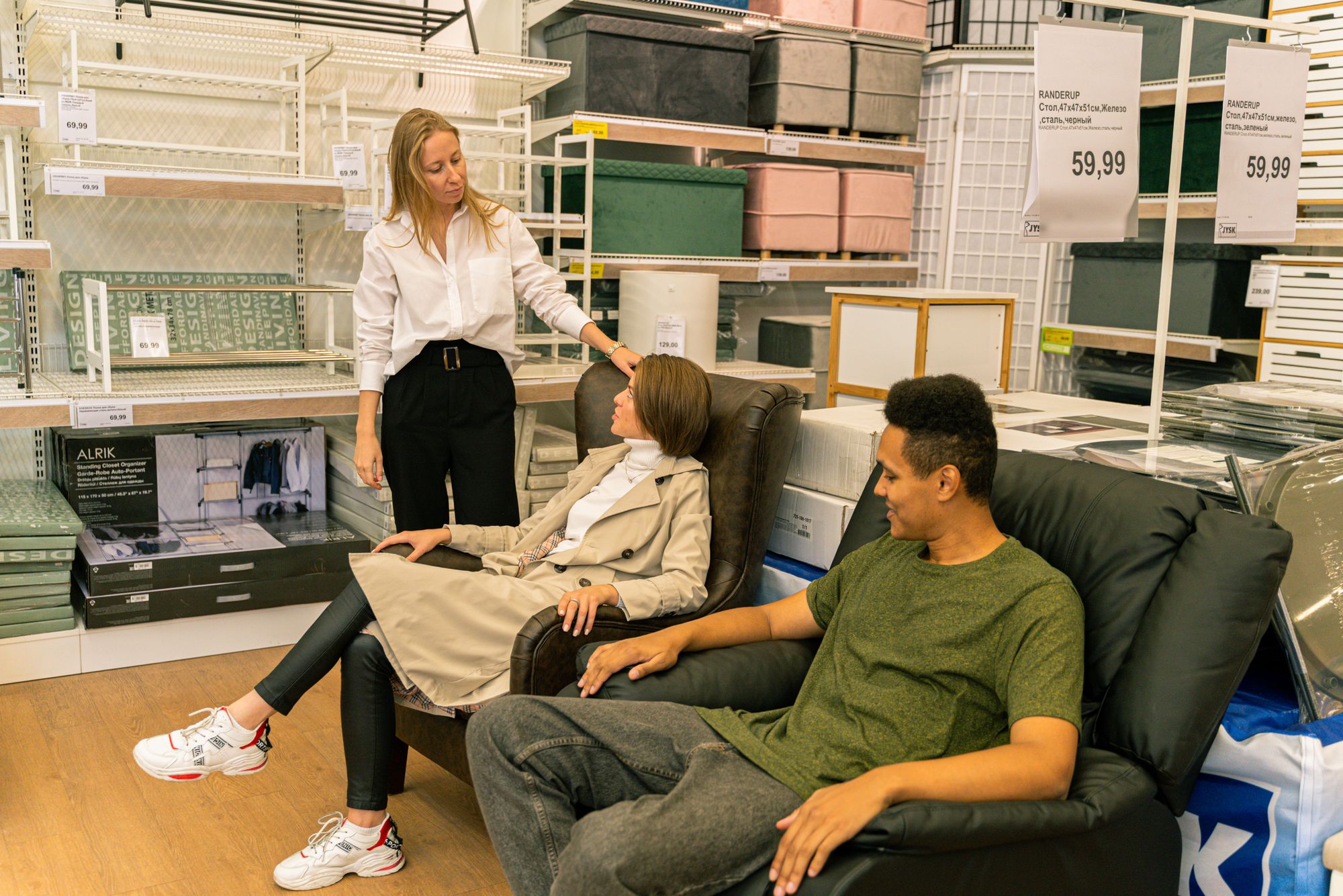 A couple testing leather chairs in a furniture store with a salesperson assisting them