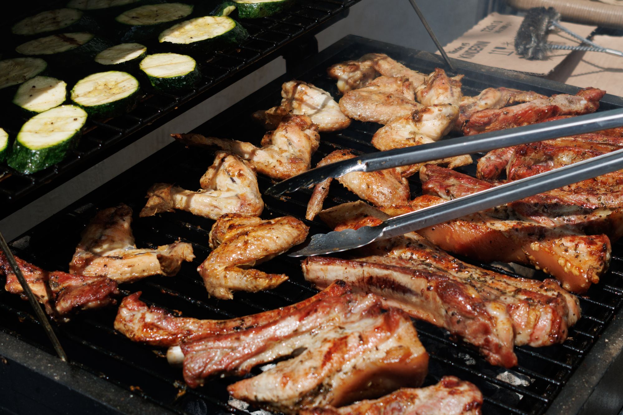 Chicken and zucchini sizzling on a lit outdoor grill during a backyard barbecue