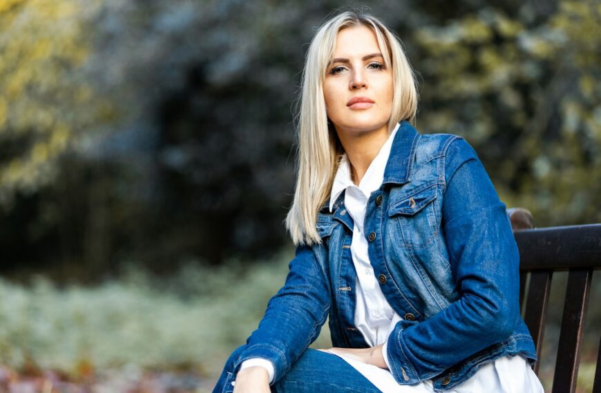woman in blue denim jacket sitting on brown wooden bench during daytime