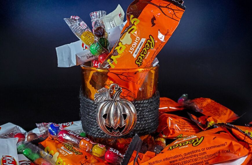 A vibrant collection of assorted Halloween candies in a glass bowl with a pumpkin decoration.