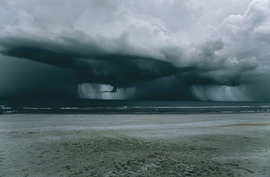 A powerful storm looms over a deserted beach, creating a dramatic skyscape.