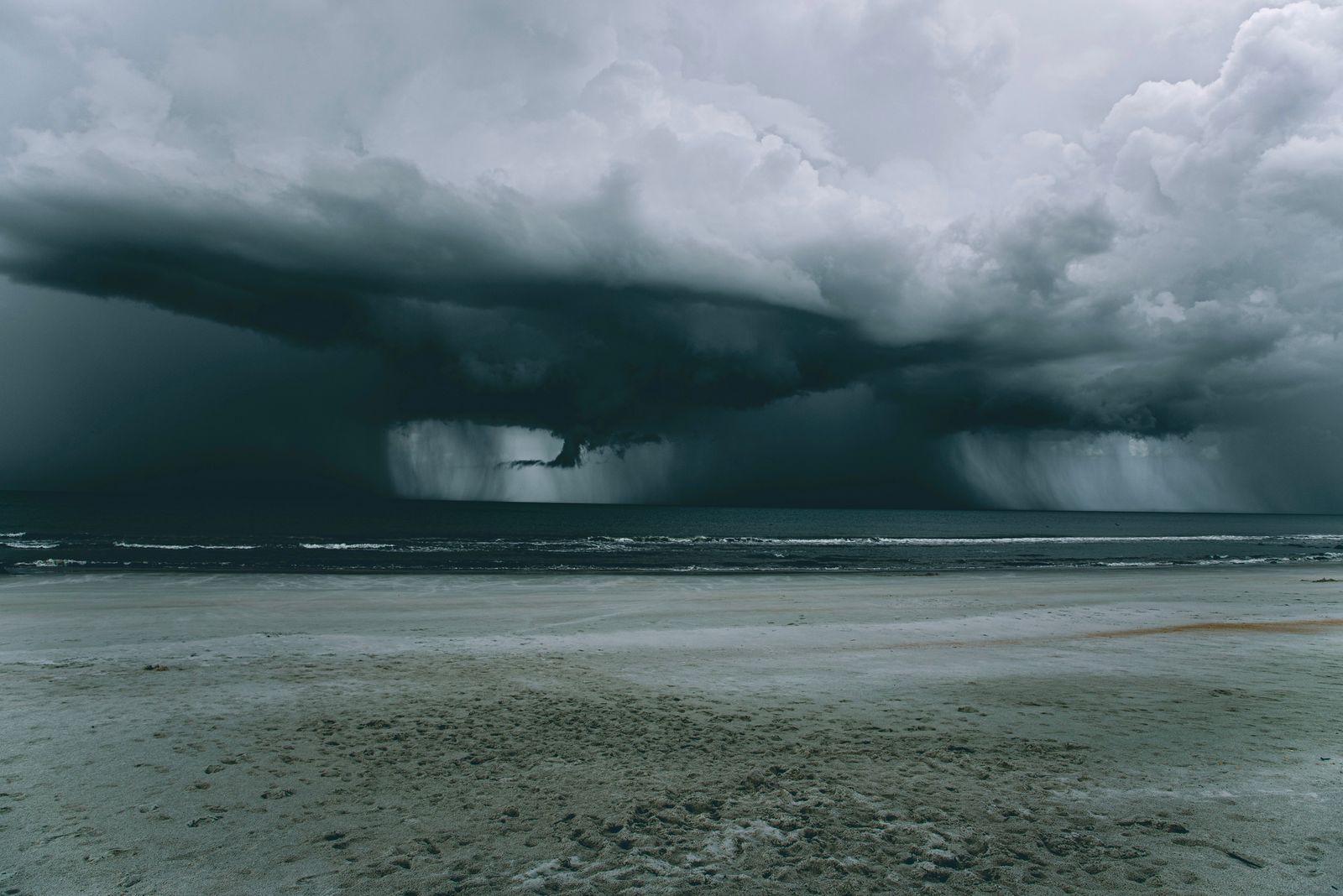 A powerful storm looms over a deserted beach, creating a dramatic skyscape.