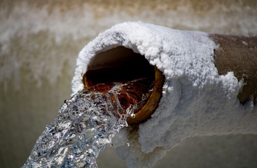 Close-up of water flowing from a rusty pipe with salt deposits, capturing motion and texture.