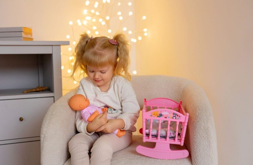 Adorable child sitting in an armchair, playing with a doll and toys in a warmly lit room.