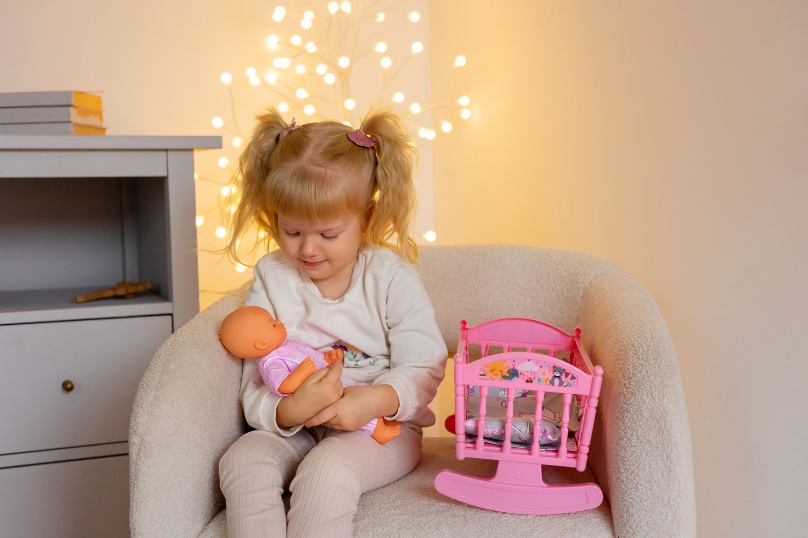Adorable child sitting in an armchair, playing with a doll and toys in a warmly lit room.
