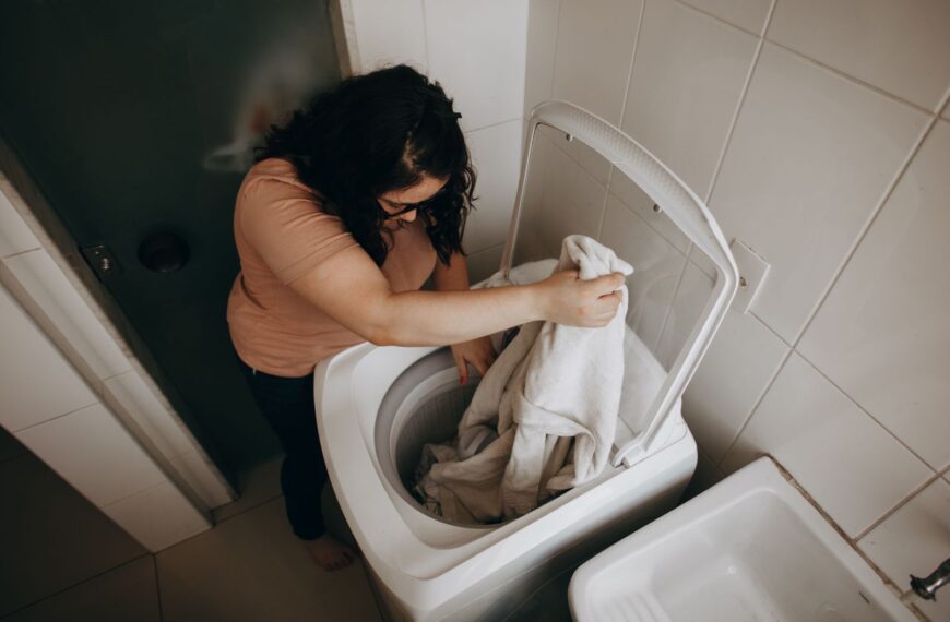 An adult woman loading clothes into a washing machine in a modern indoor space.