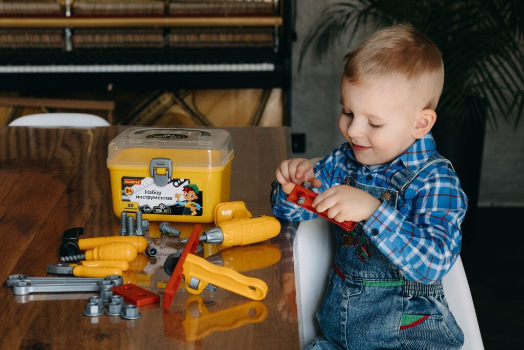A young boy plays with a colorful toy tool set on a table indoors, having fun.