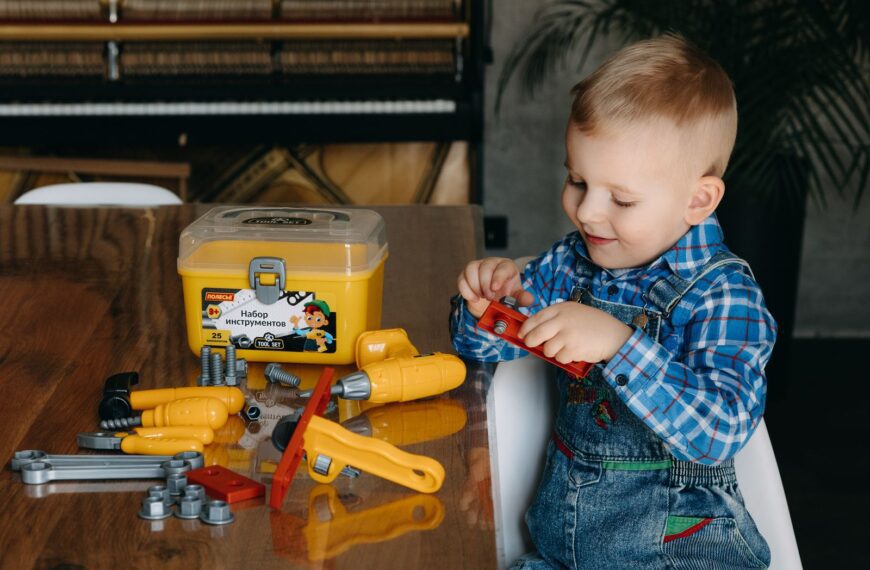 A young boy plays with a colorful toy tool set on a table indoors, having fun.
