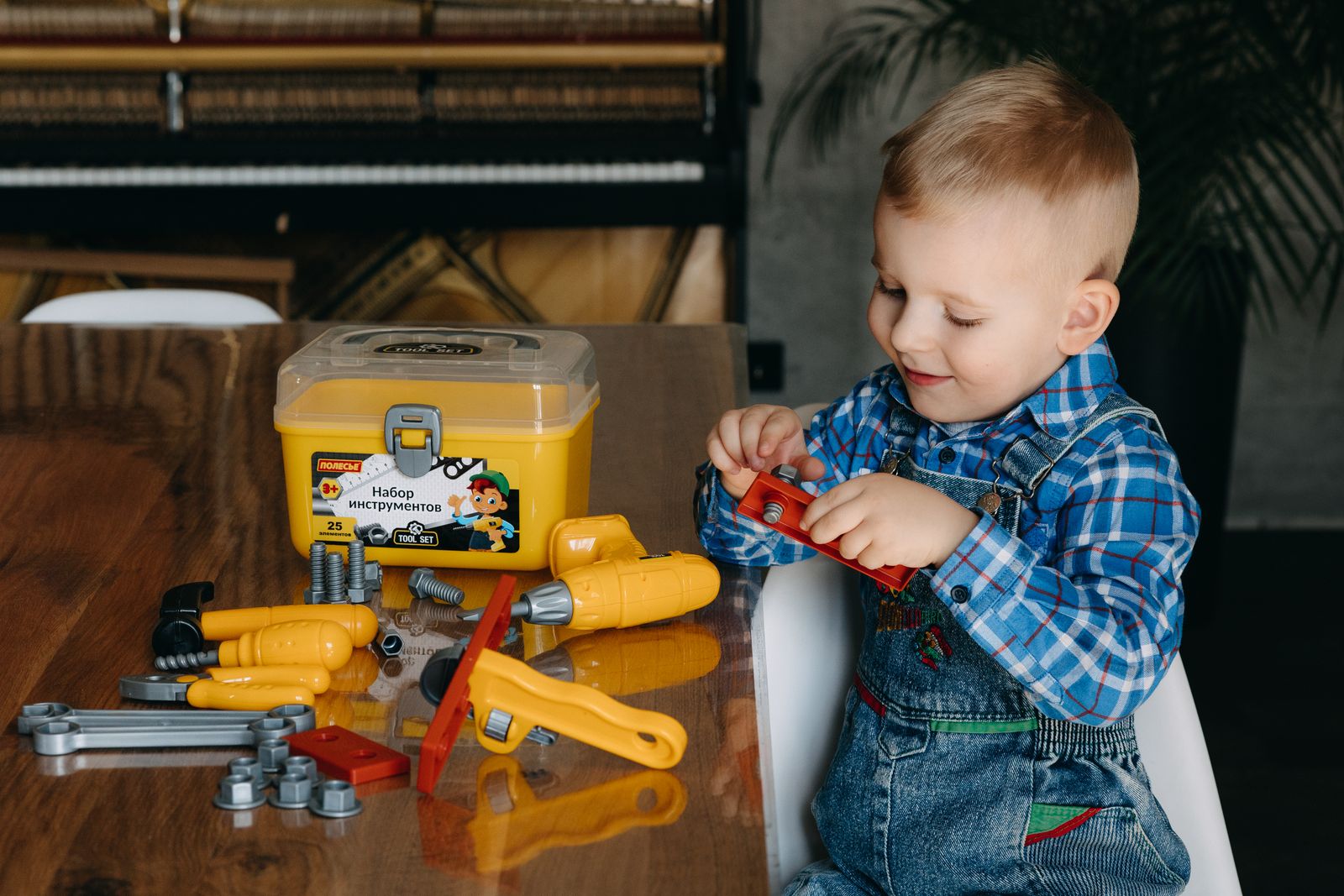 A young boy plays with a colorful toy tool set on a table indoors, having fun.