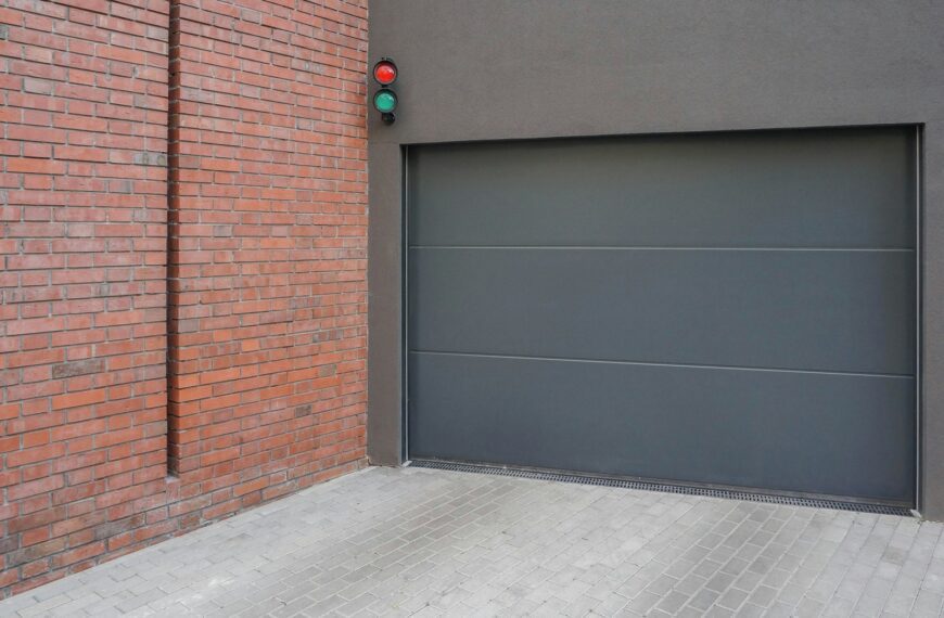a grey garage door next to a brick wall