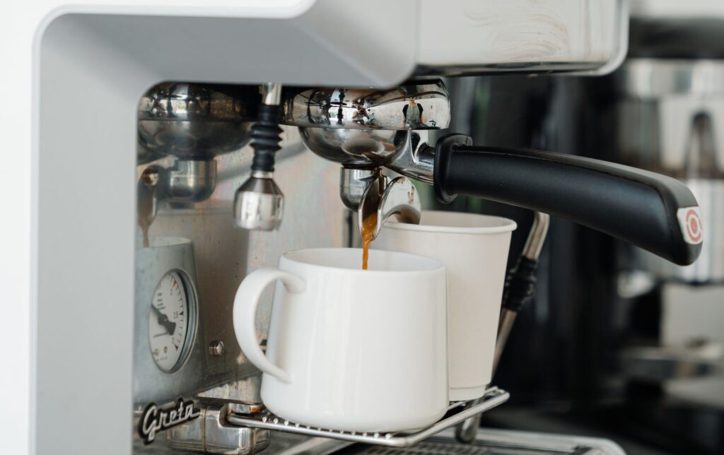 Coffee machine pouring fresh brewed aromatic coffee into ceramic mug and disposable cup